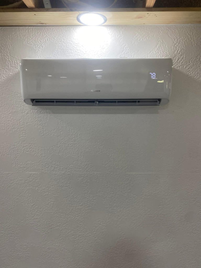 White ductless air conditioning unit mounted on textured wall with recessed ceiling light above