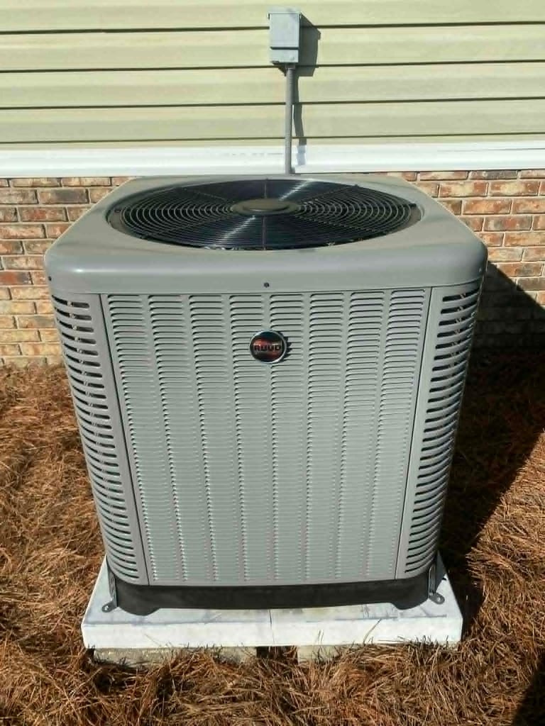 Outdoor air conditioning unit installed against brick wall with metal conduit running upward
